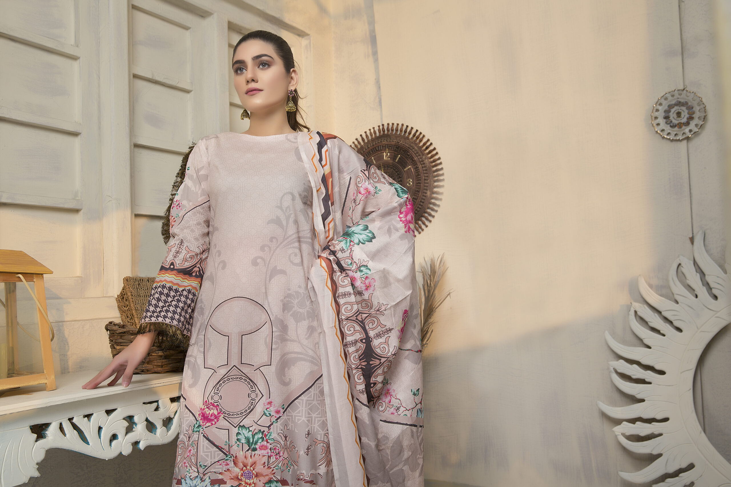 Rajvansh - Best Unstitched Suit Fabric for Women for Every Occasion - Rajvansh Woman in a pale beige dress with floral print poses indoors against carved white decor and a round wall ornament.