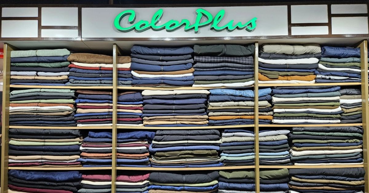 Readymade Garment Store for Traditional and Casual Wear - Rajvansh Shelves of neatly folded jeans and pants in many colors under a neon ColorPlus sign in a clothing store