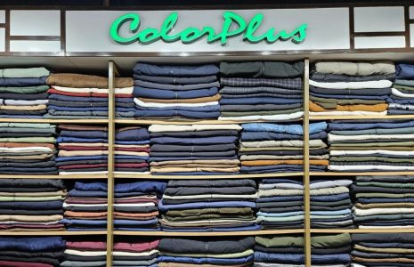 Shelves of neatly folded jeans and pants in many colors under a neon ColorPlus sign in a clothing store